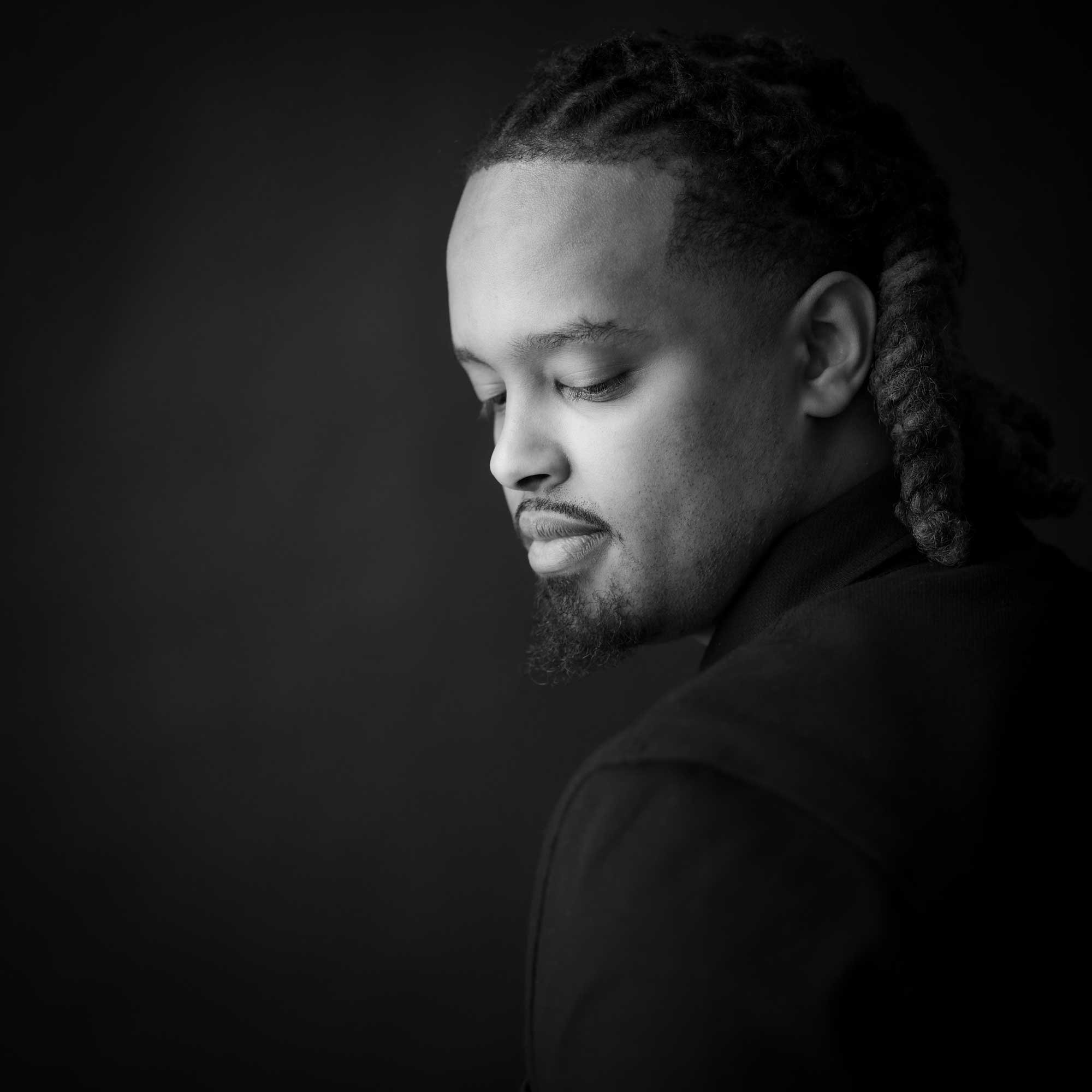 Black-and-white portrait of a man with neatly braided hair, a goatee, and a contemplative expression, by Jerome Art Photography.