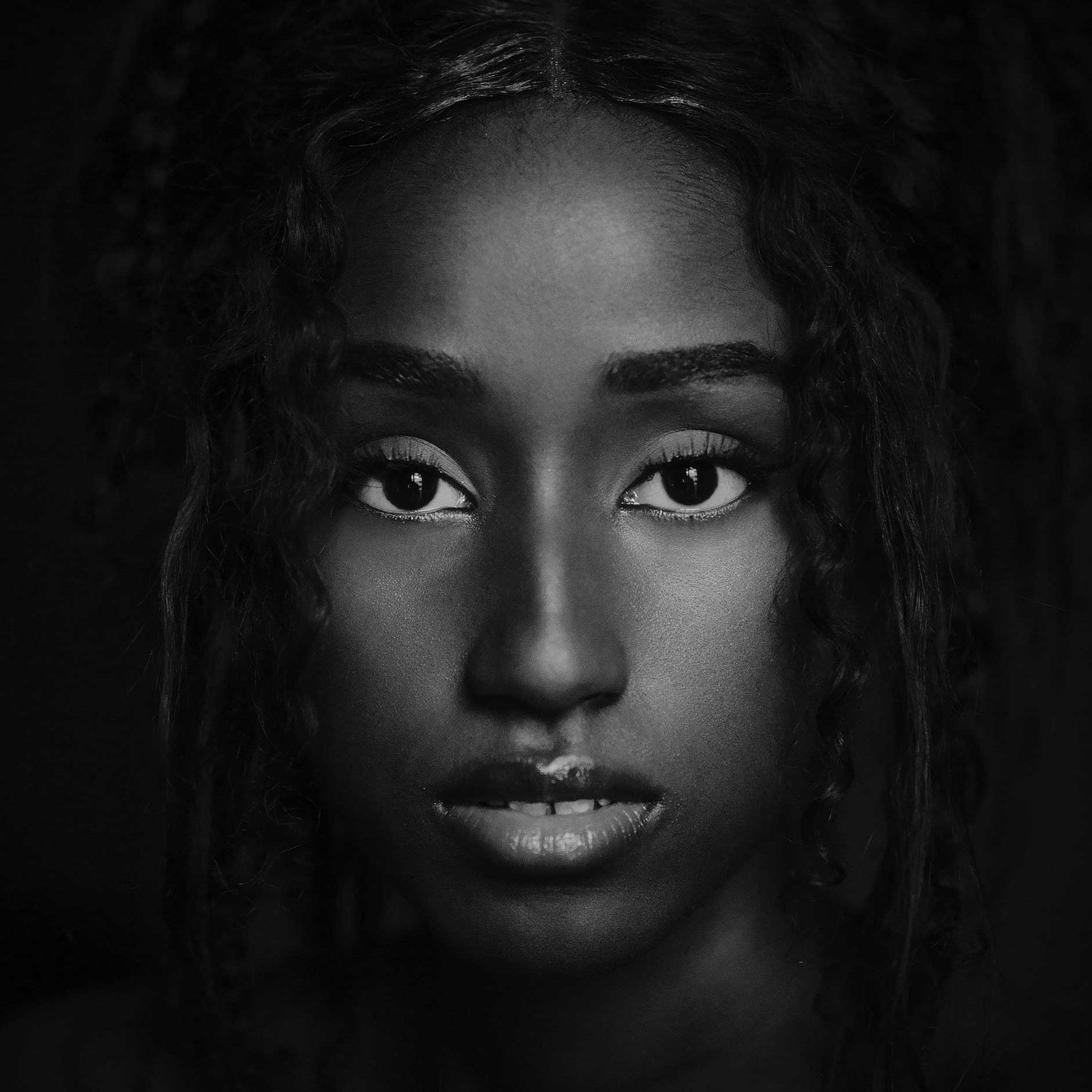 Close-up black-and-white portrait of a young Black woman with intense gaze and curly hair, studio lighting