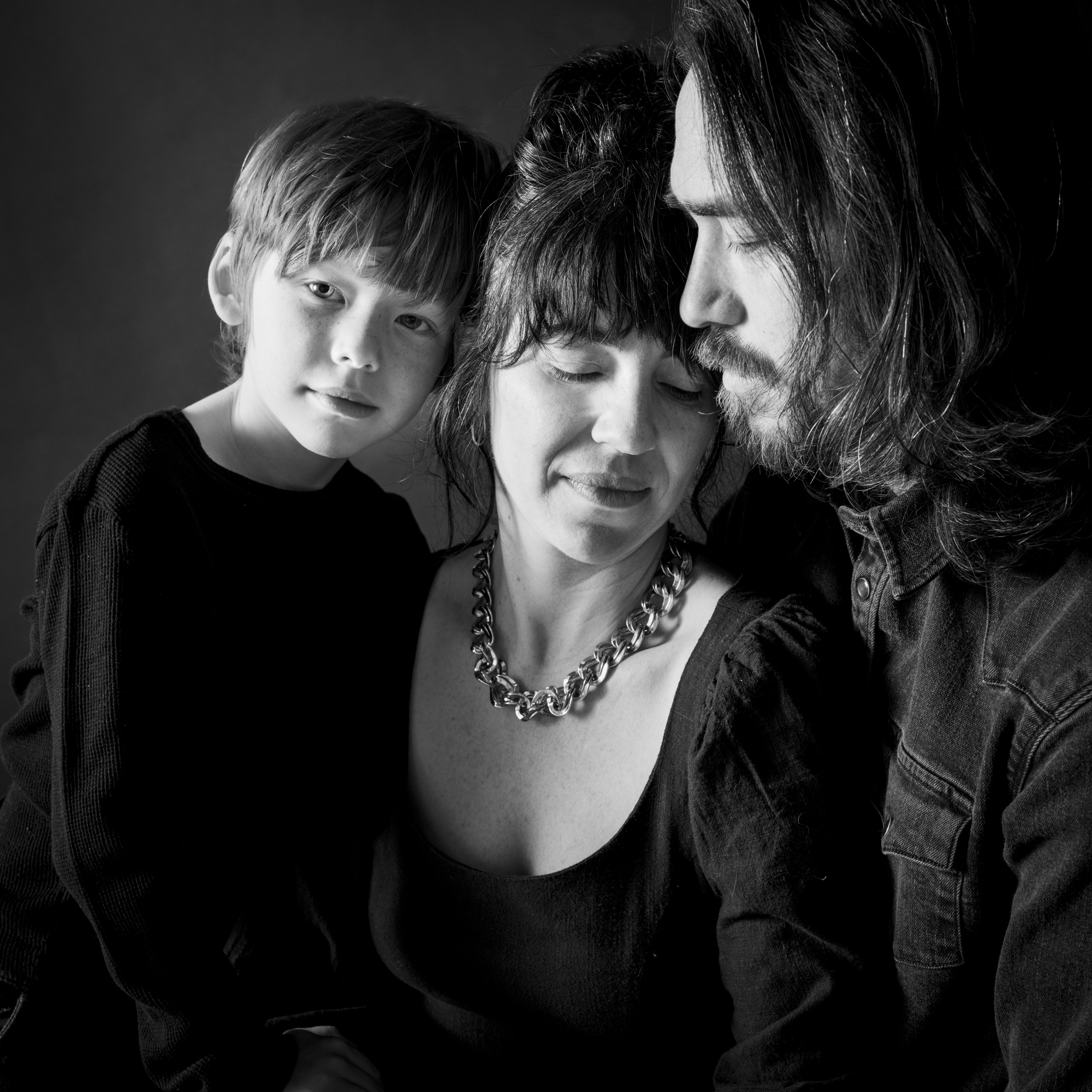 Portrait en noir et blanc d'une famille de trois personnes, avec un jeune garçon penché sur ses parents, capturant un moment intime et affectueux, par Jerome Art Photography.