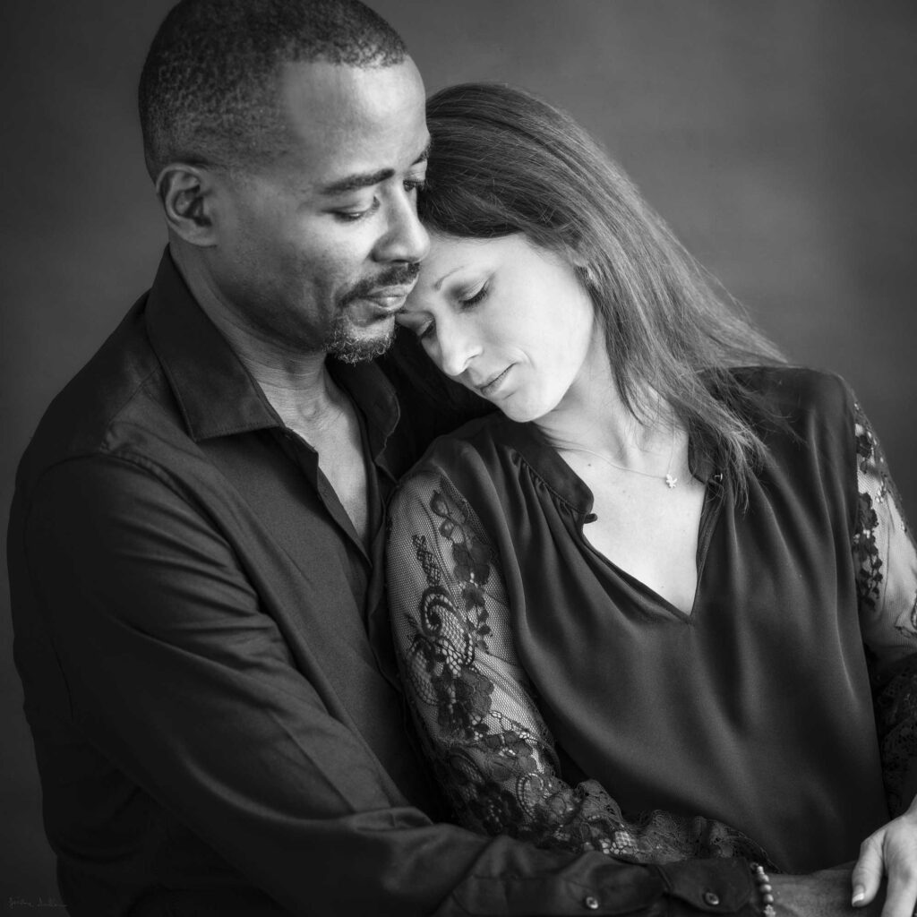 Black and white fine art portrait of a couple in a tender embrace, photographed in studio.