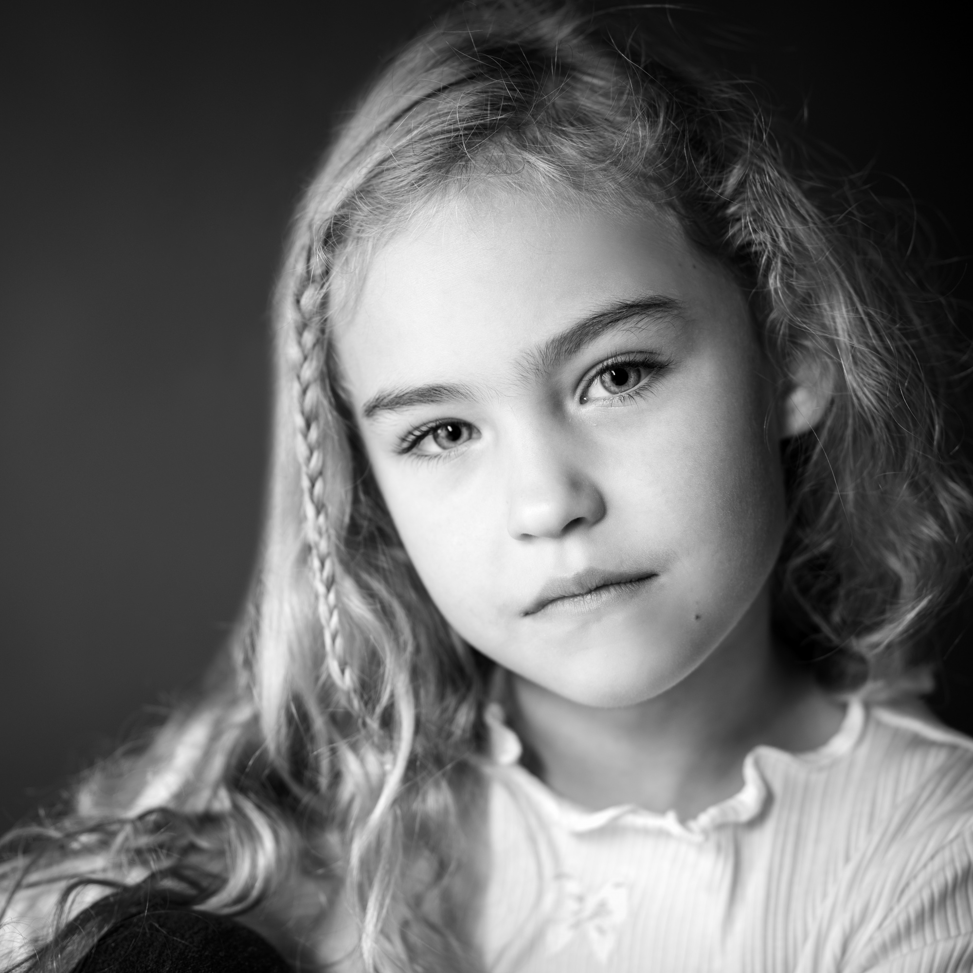 Portrait en noir et blanc d'une jeune fille aux longs cheveux blonds ondulés et au regard doux et introspectif, par Jerome Art Photography.