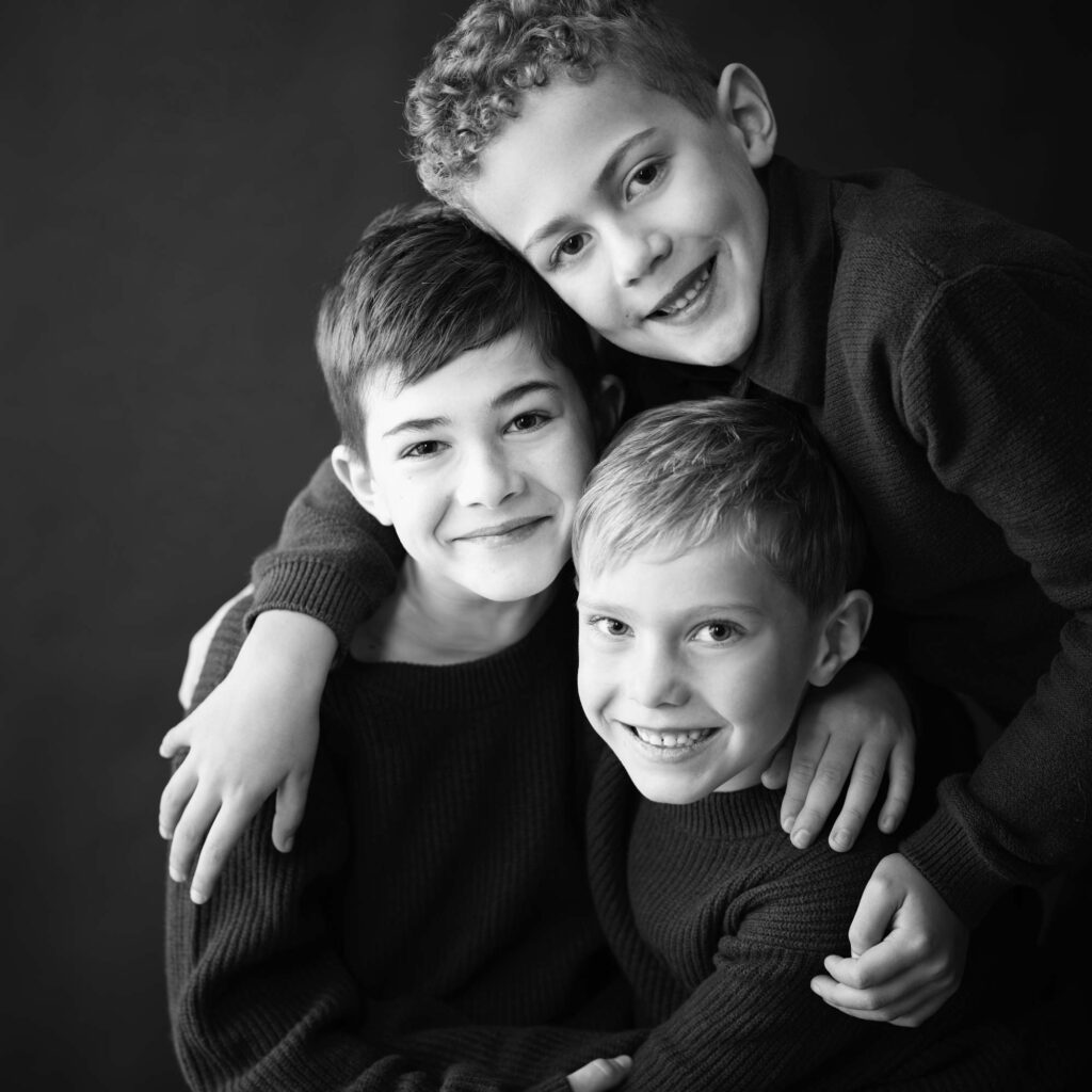Trois jeunes frères souriants s'embrassant dans un portrait de studio en noir et blanc