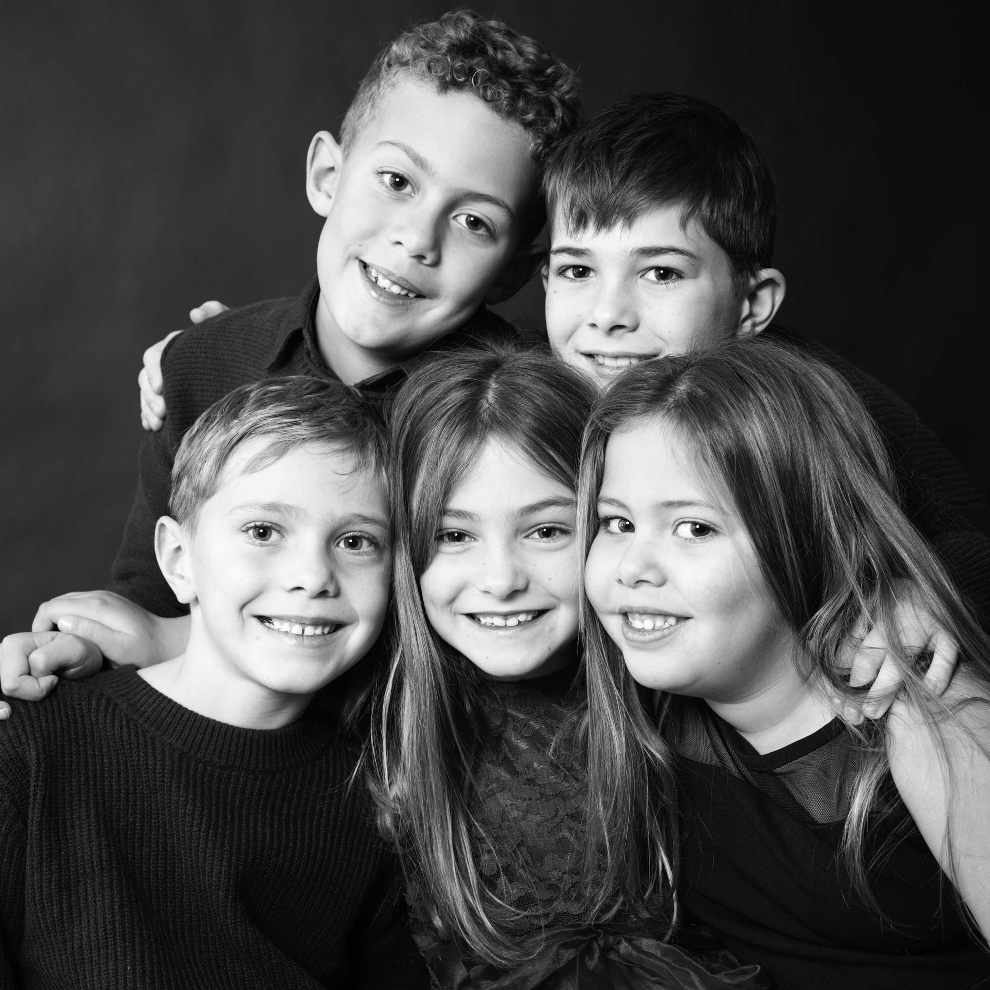 Black and white studio portrait of five smiling children closely huddled together