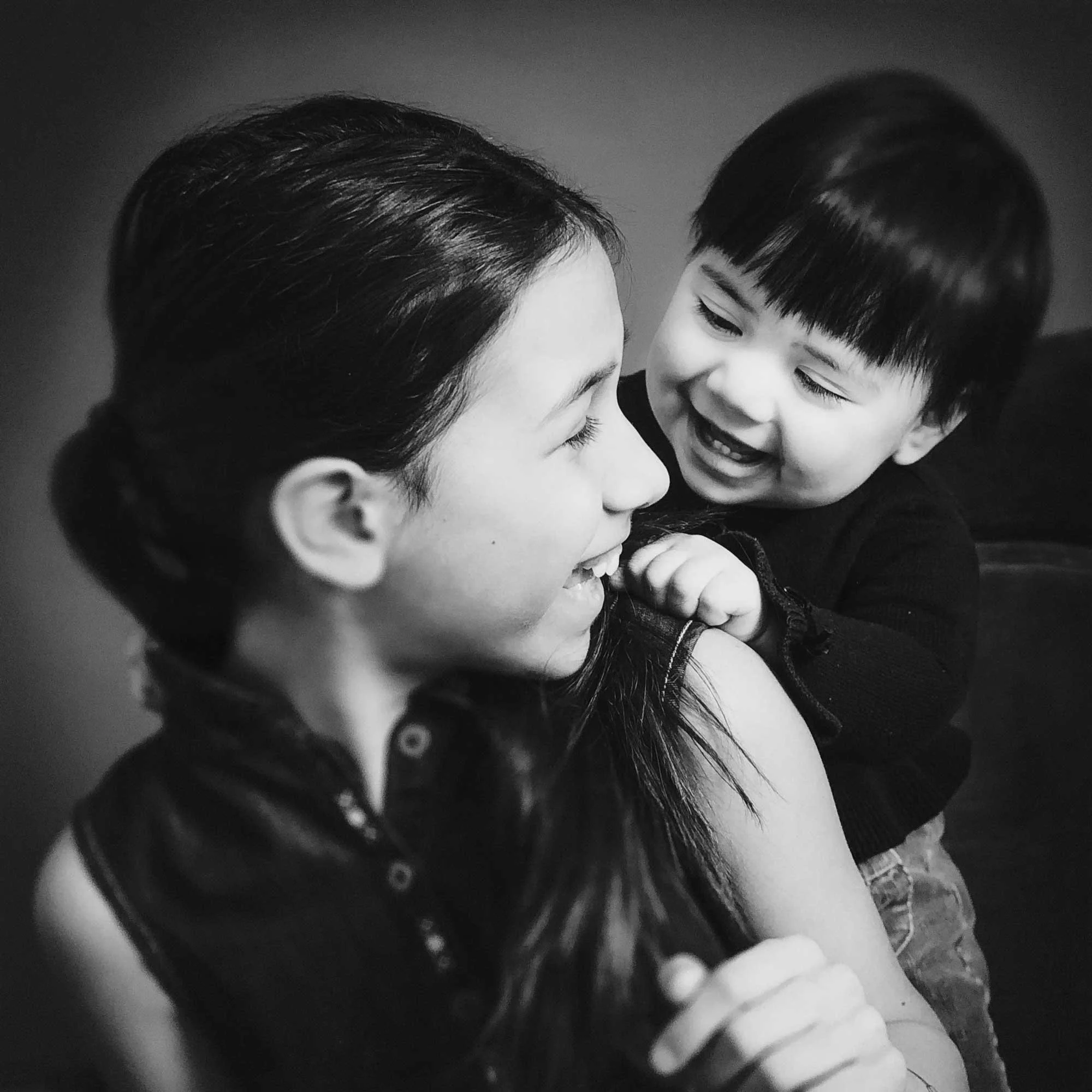 Portrait en noir et blanc de deux sœurs partageant un moment de joie, la plus âgée tenant la plus jeune sur son épaule