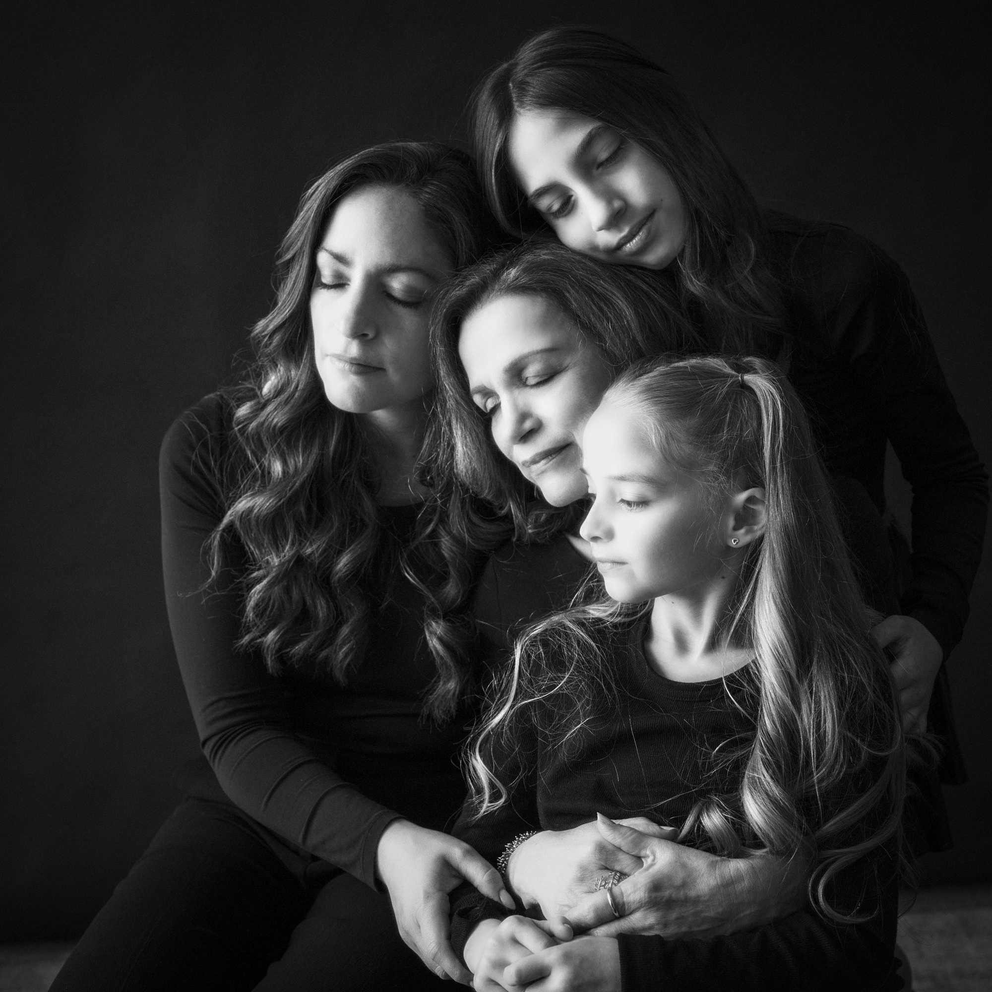 Black and white portrait of three generations of women embracing with eyes closed, expressing connection and legacy