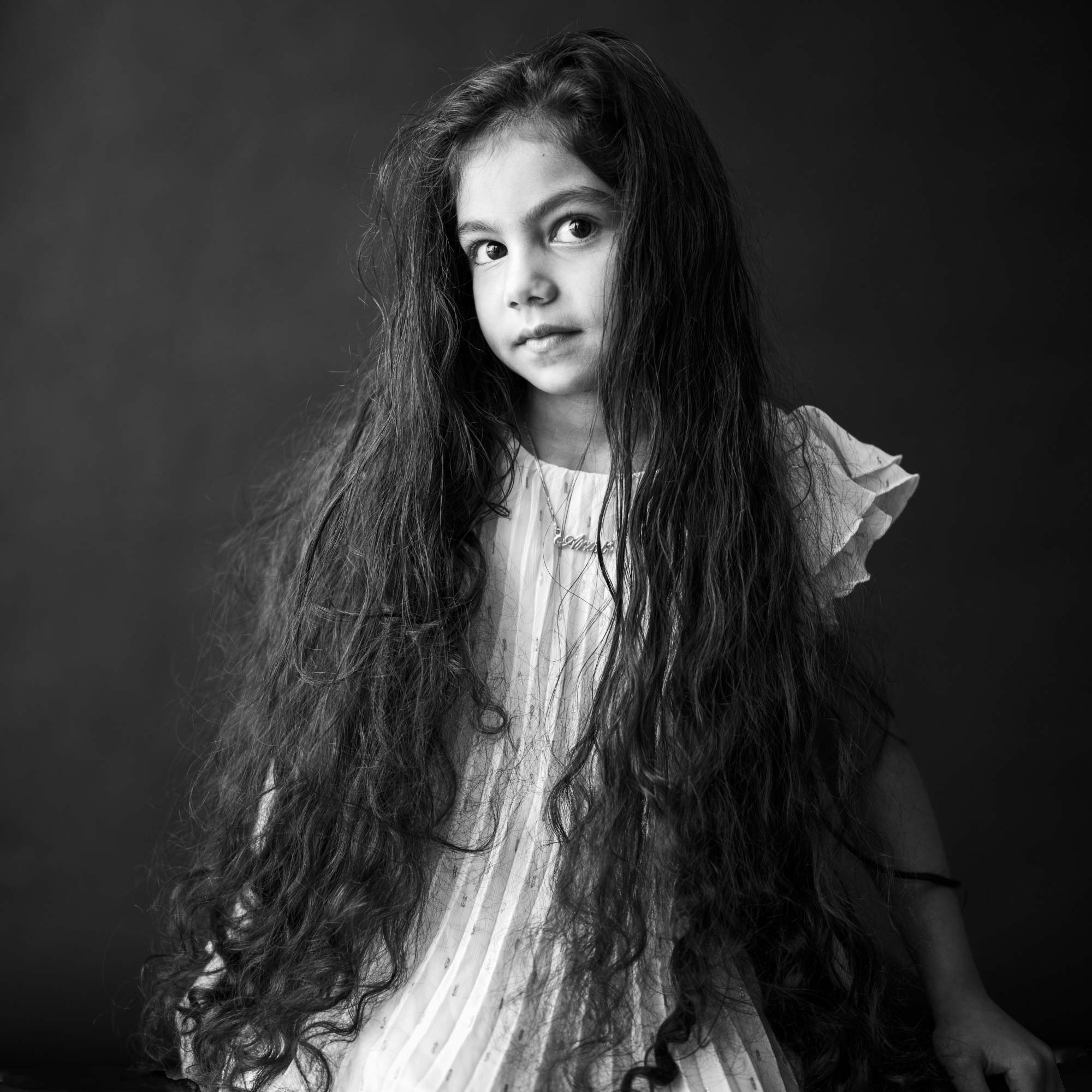 Portrait en noir et blanc d'une jeune fille aux cheveux longs et ondulés portant une robe blanche, par Jerome Art Photography.