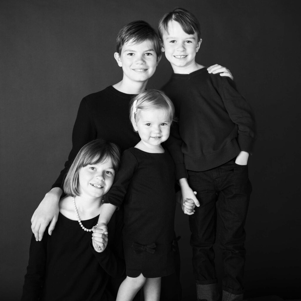 Portrait de studio en noir et blanc de quatre frères et sœurs, souriants et se tenant par la main, symbolisant l'amour de la famille et l'unité.