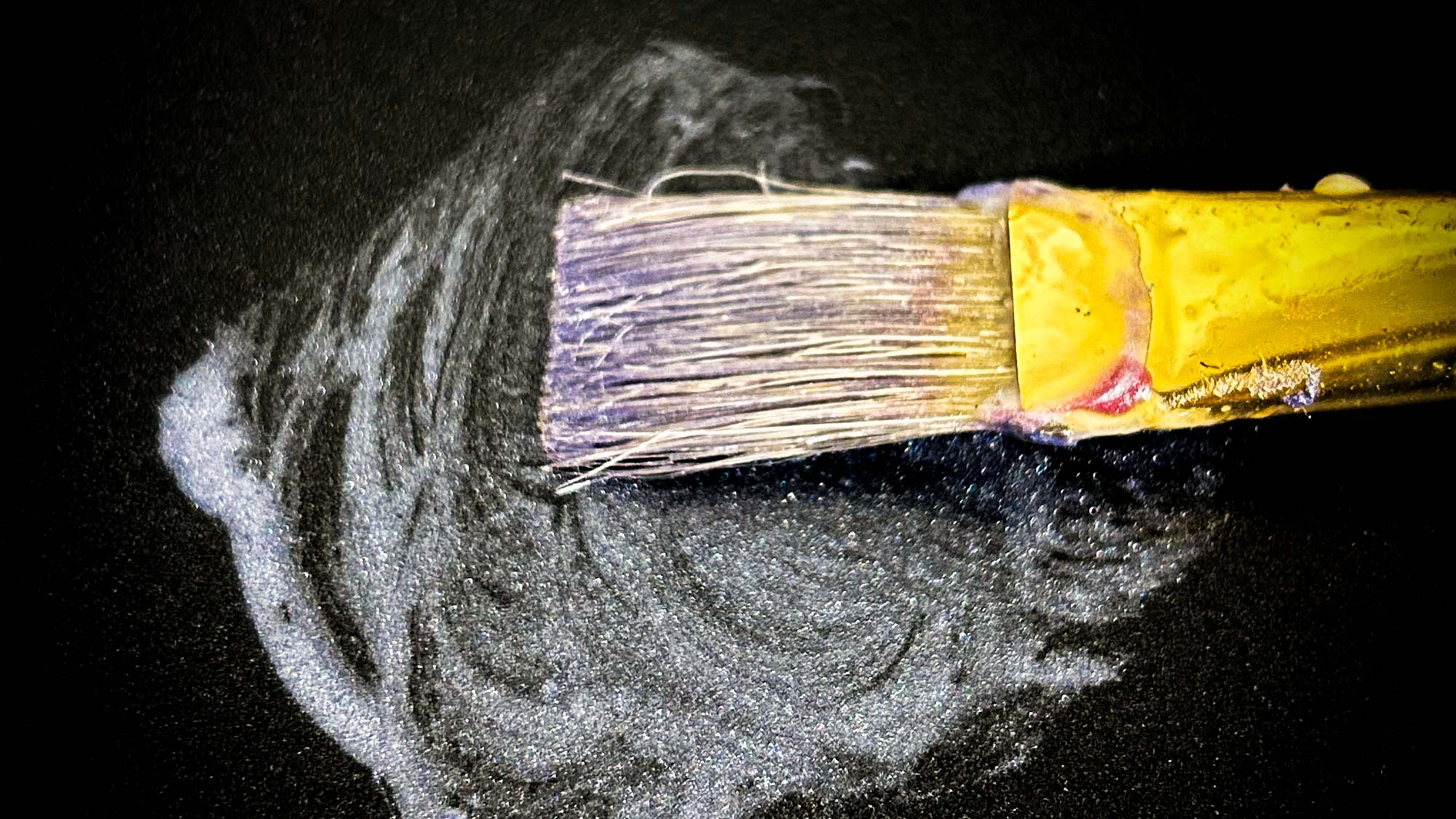 Close-up of a paintbrush spreading beeswax and oil in circular strokes on a dark surface.