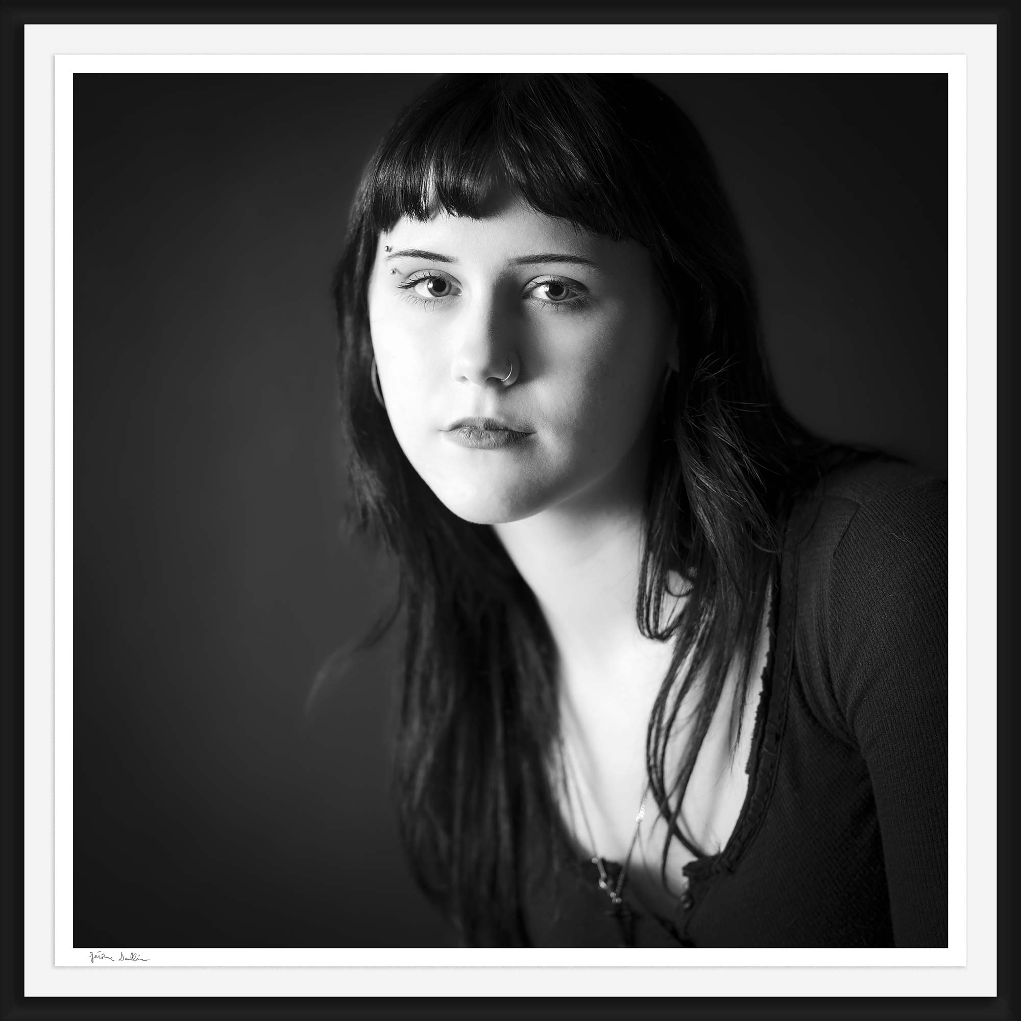 Award winning framed black and white portrait of a young woman with dark hair, eyebrow piercing and nose ring, softly lit against a dark background, showcasing Jérôme Scullino’s signature fine art portrait style.