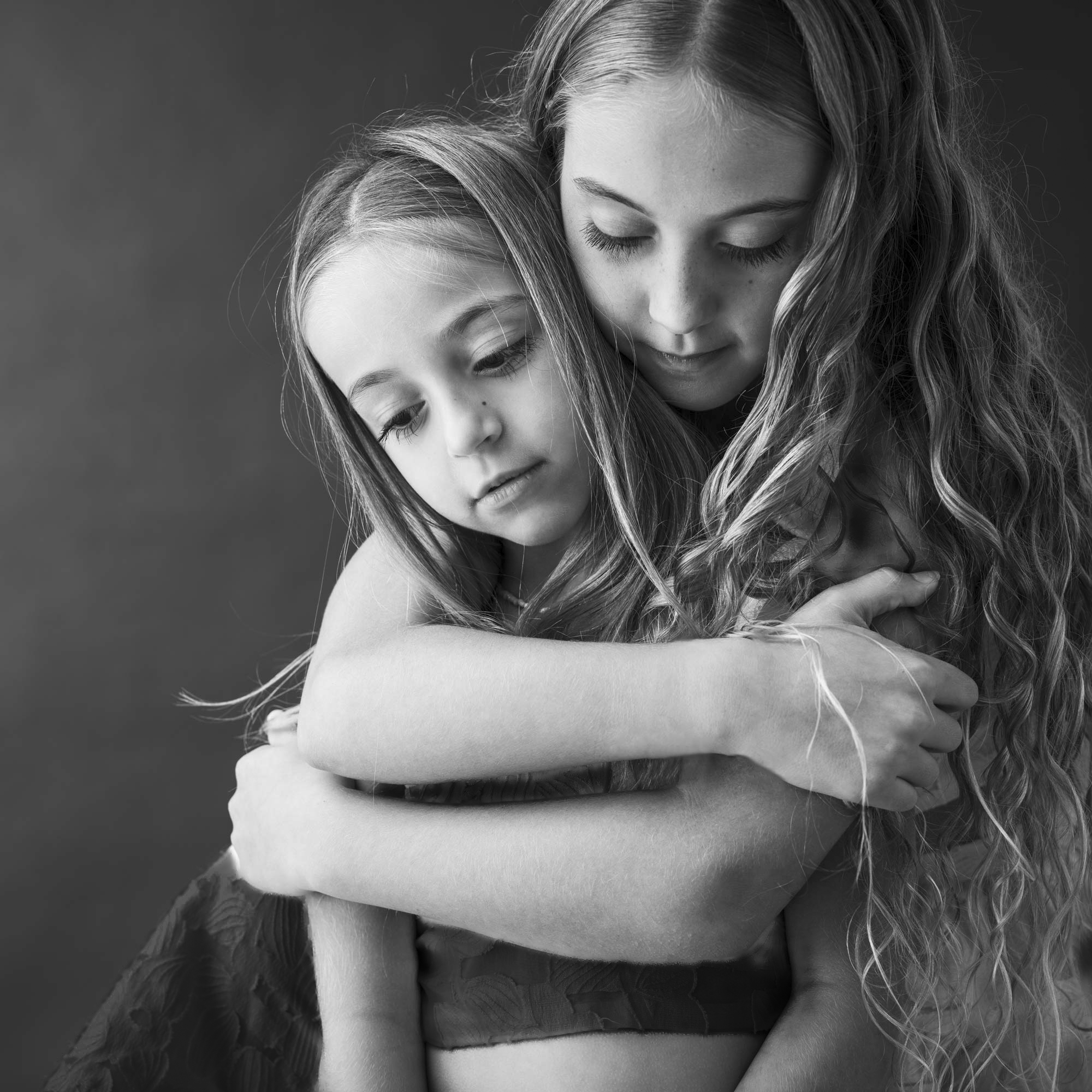 Two young sisters embracing in a monochrome portrait by Jérôme Scullino